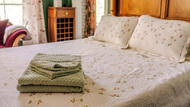 A neatly made bed with a folded blanket, floral-patterned pillows, and a wooden nightstand with a tissue box.