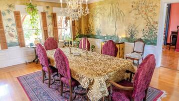 Une salle à manger avec une grande table, des chaises décorées, un lustre et une fresque murale.