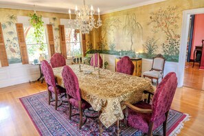 Un comedor con una mesa grande, sillas ornamentadas, una araña y un mural en la pared.