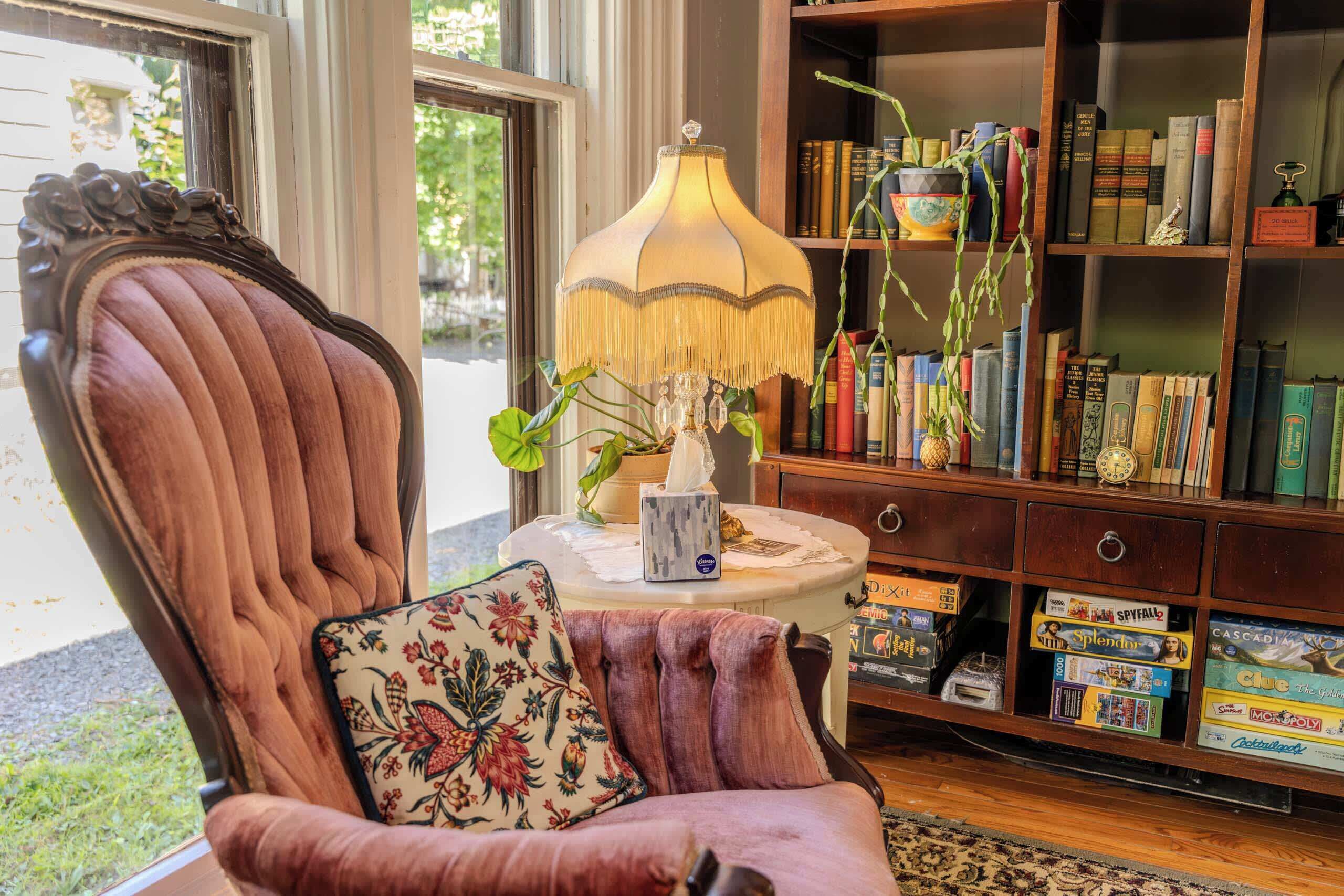 A room with a plush armchair, a lamp, a bookshelf, and a window.