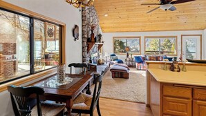 Une cuisine spacieuse avec des meubles de rangement en bois, un coin repas avec une table et des chaises en bois, et de grandes fenêtres offrant une vue sur l’extérieur.