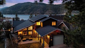 Une maison en rondins moderne dotée d’un garage, d’un espace extérieur aménagé et offrant une vue sur un lac et des montagnes.