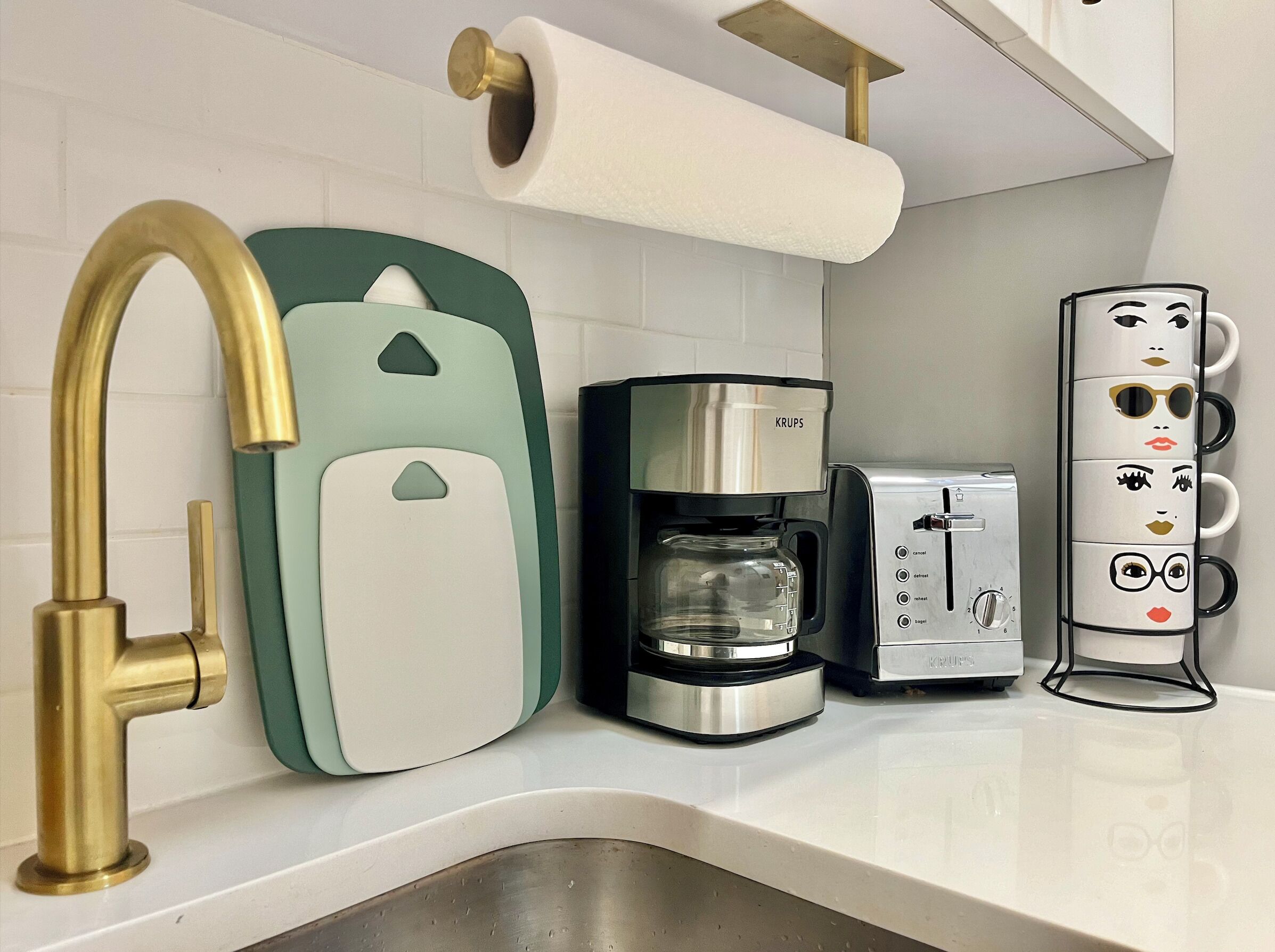 Une cuisine moderne équipée d’une machine à café en acier inoxydable, d’un grille-pain Krups et d’un appareil électroménager vert et blanc.