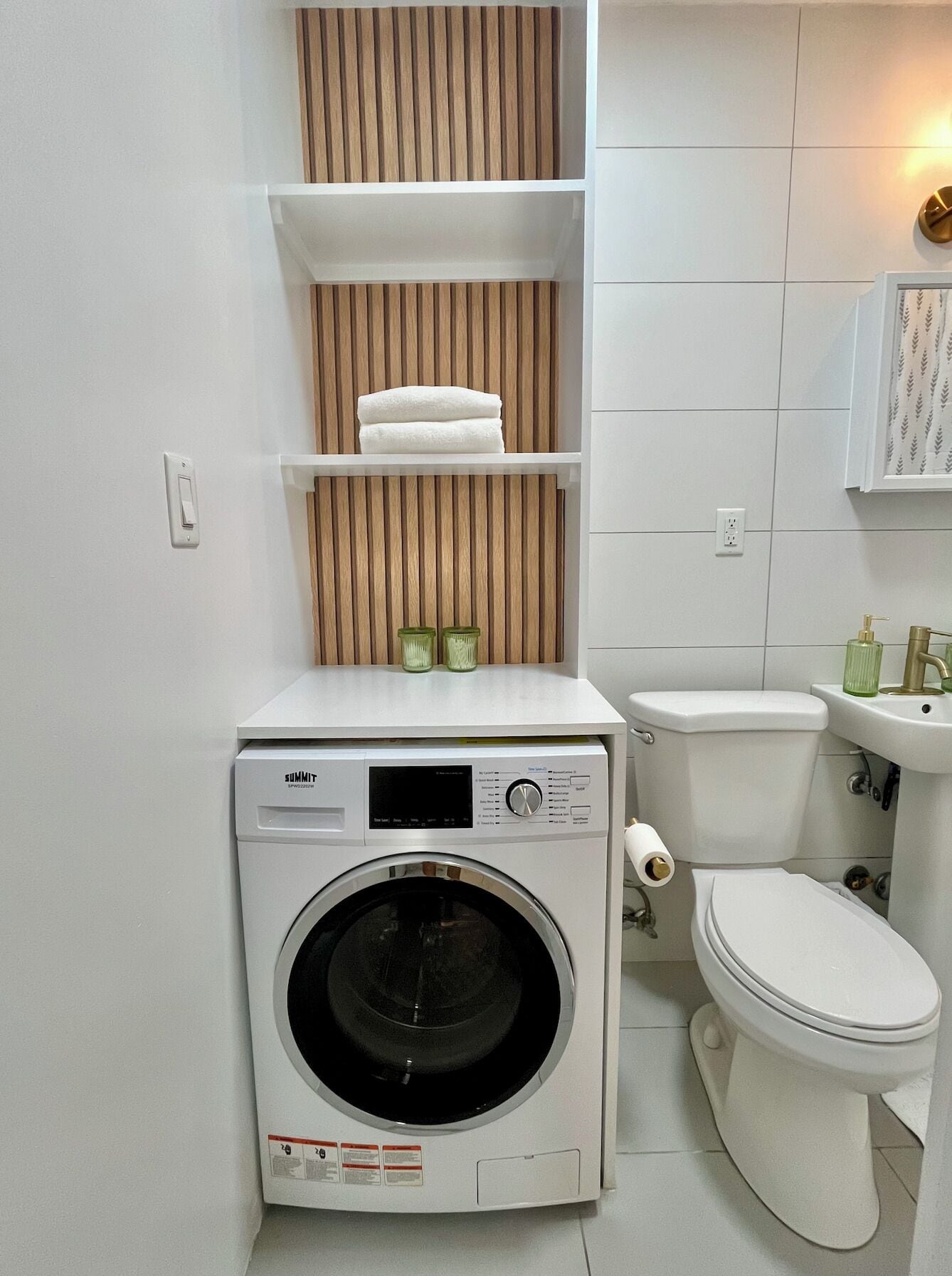 Un baño compacto y moderno con lavadora incorporada, inodoro y un lavamanos pequeño.