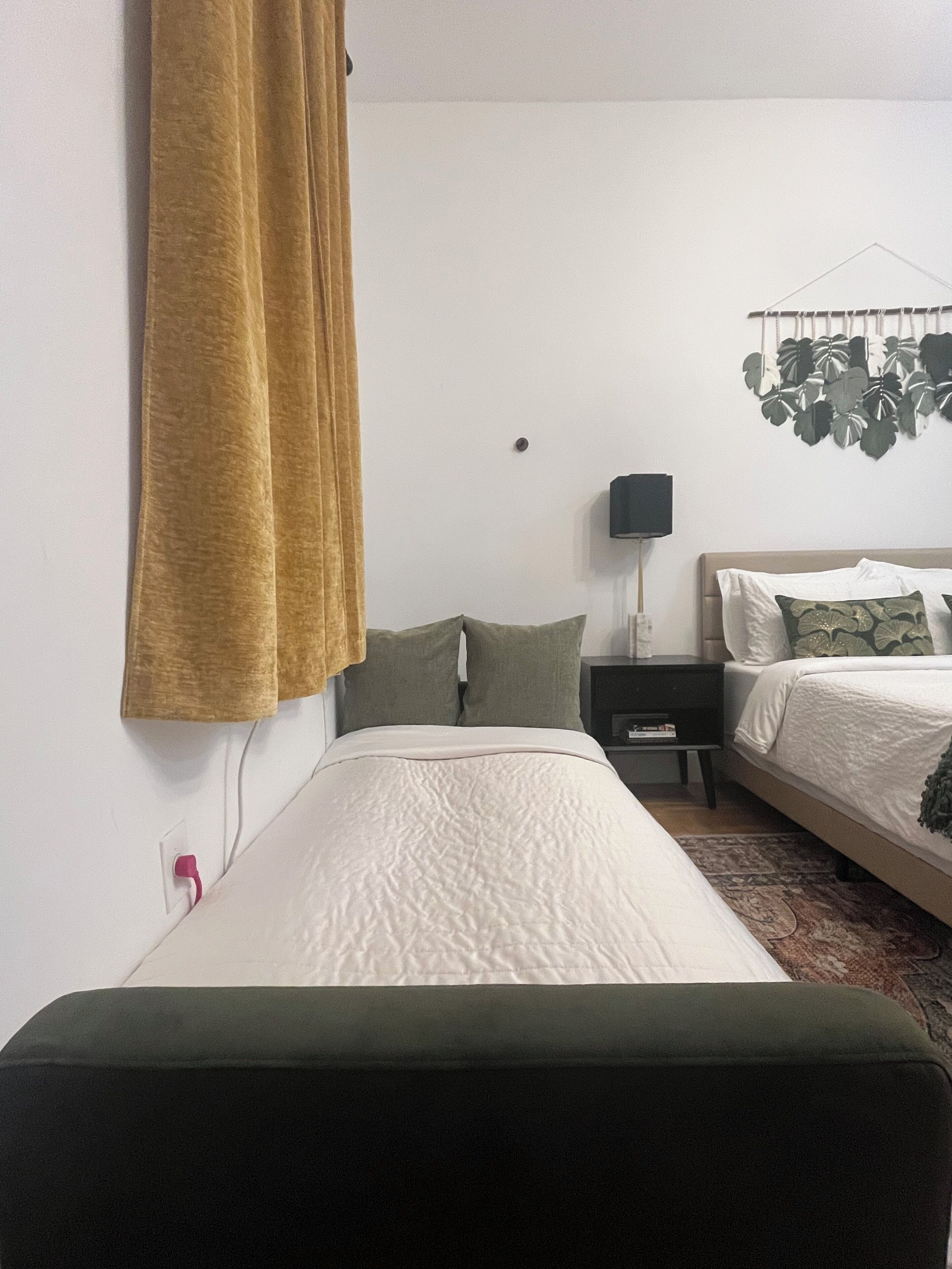 Un dormitorio con cama, mesita de noche, lámpara y una planta colgante.
