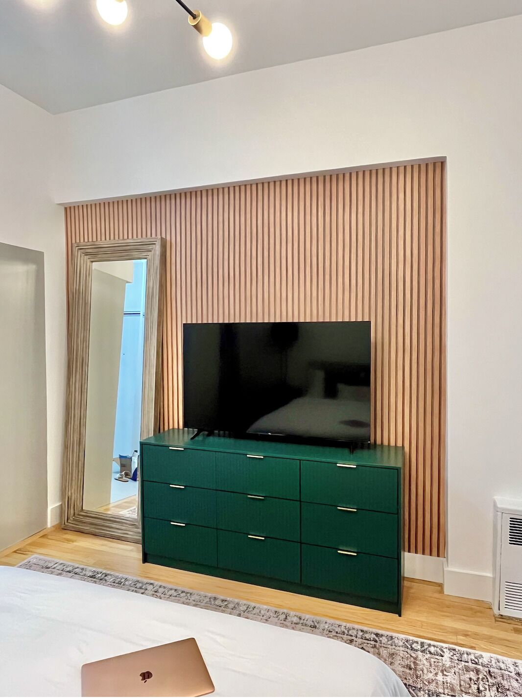 A bedroom with a large mirror, a green dresser, a flat-screen TV, and a bed.