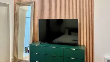 A bedroom with a large mirror, a green dresser, a flat-screen TV, and a bed.
