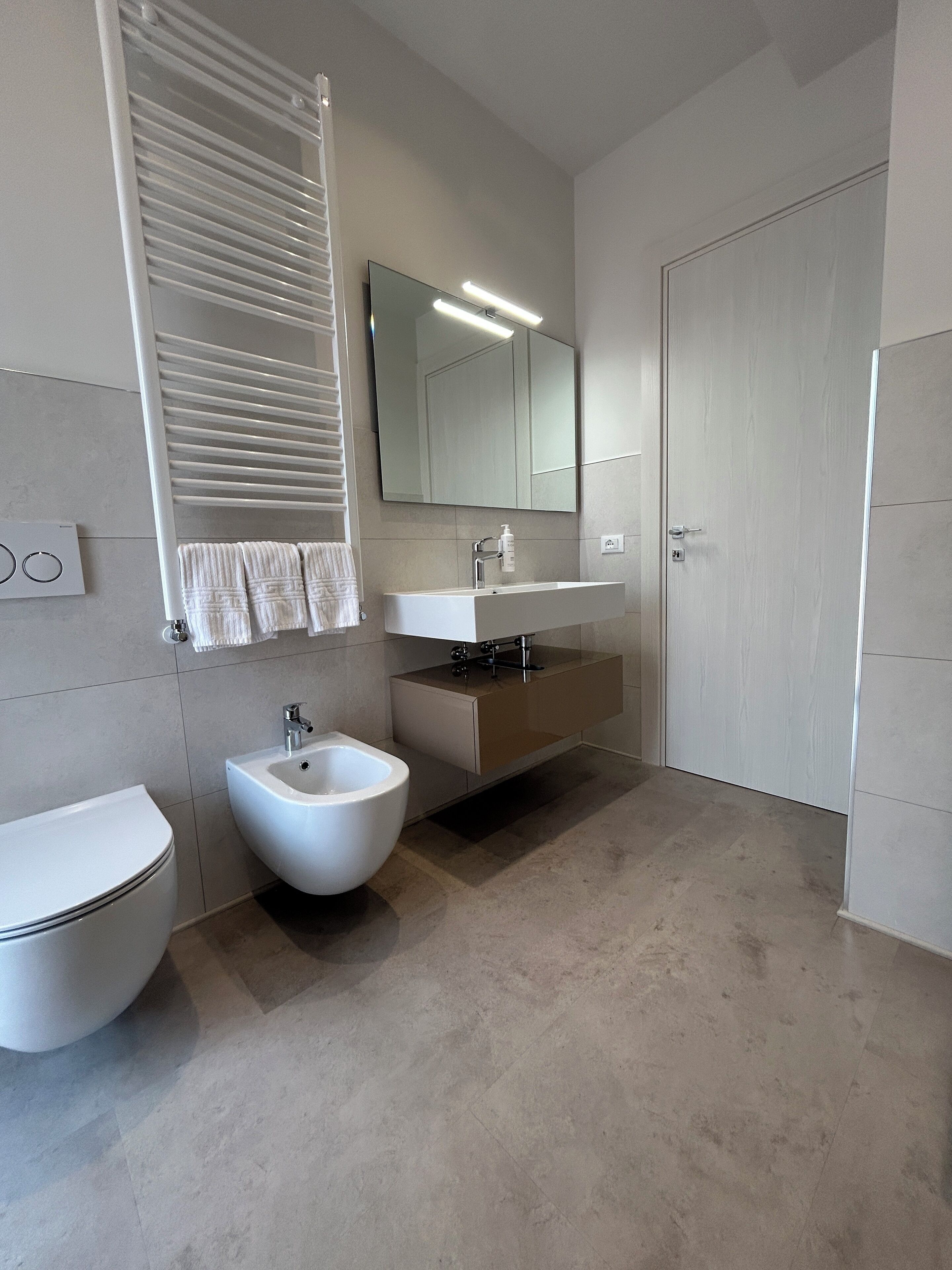 A modern bathroom with a toilet, bidet, sink, and mirror.