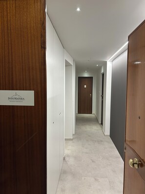 A corridor with a wooden door on the left, a sign reading 'INTO MATERA BUSINESS APARTMENTS,' and a door at the end. - IntoMatera business apartments (Matera)