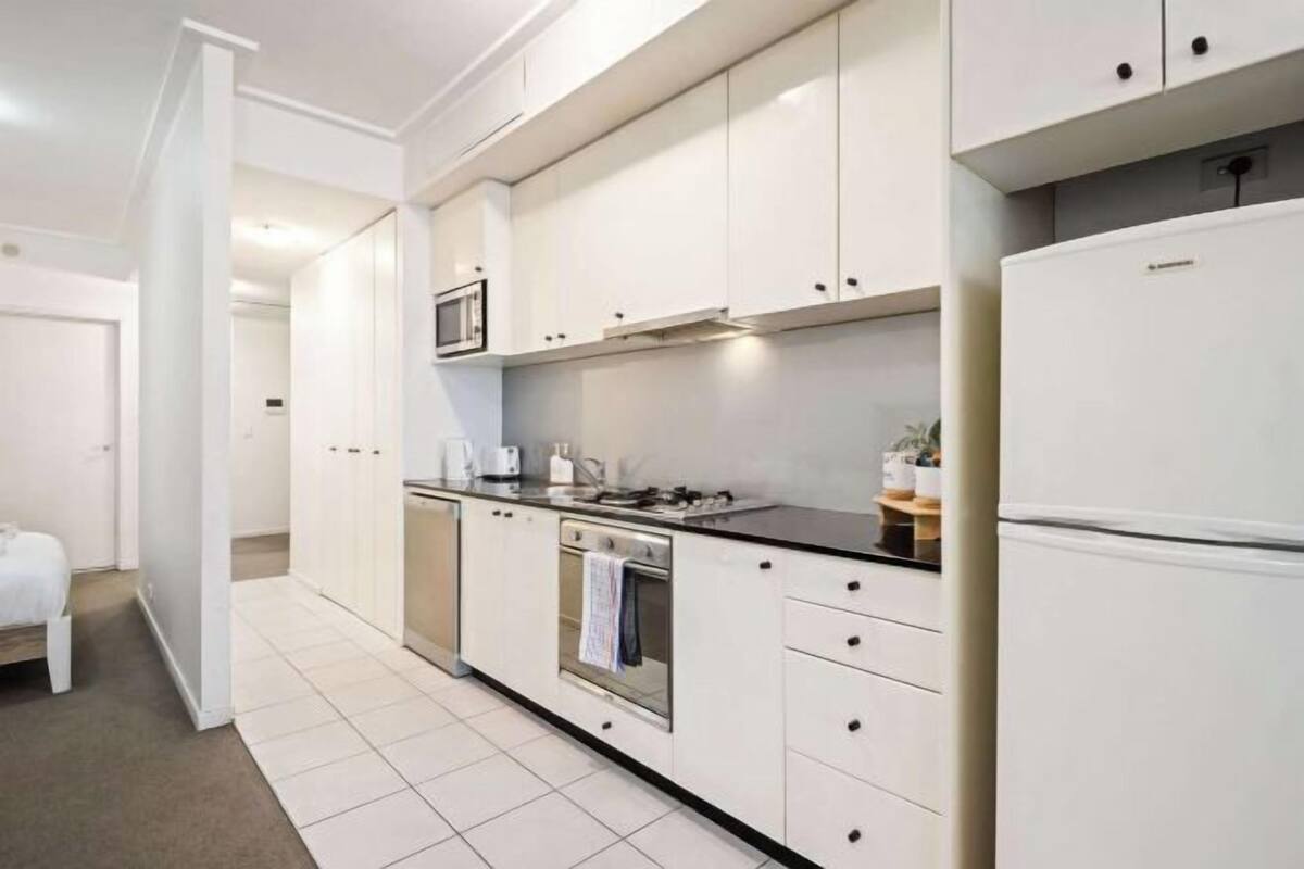 A modern kitchen with white cabinets, a black countertop, a built-in oven, and a refrigerator.