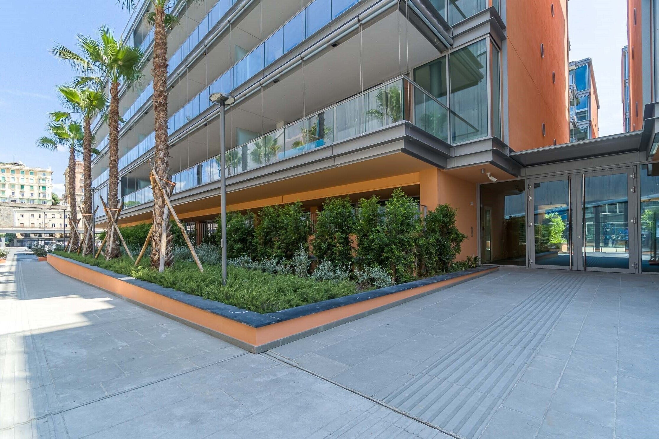 Un bâtiment moderne doté d’une façade en verre, d’un espace extérieur aménagé pour s’asseoir et de palmiers.