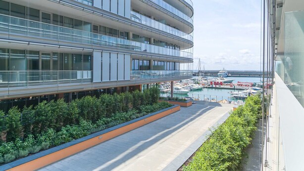 Un edificio moderno con varios balcones que dan a un puerto deportivo con barcos.