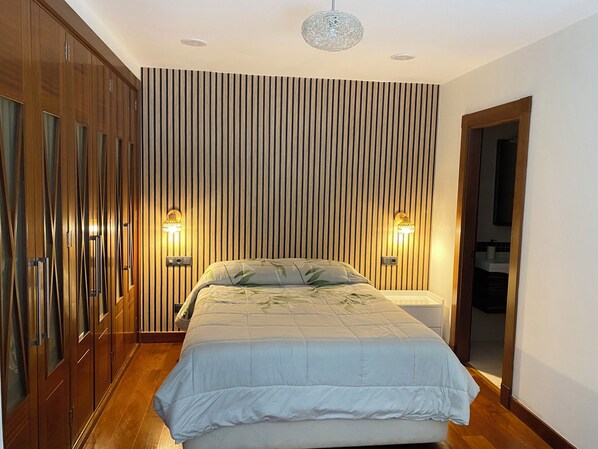 Un dormitorio con cama, armario de madera y dos lámparas fijadas a la pared.
