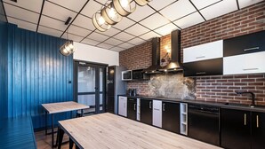 A modern kitchen with a brick backsplash, stainless steel appliances, and wooden tables. - VOLA Hostel (Warsaw)