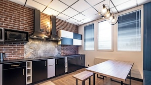 A modern kitchen with a brick backsplash, a built-in microwave, and a large window with blinds. - VOLA Hostel (Warsaw)
