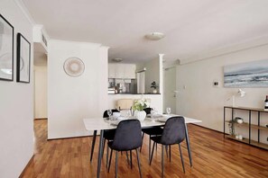 A modern dining area with a white table set for four, black chairs, a vase with flowers, and a clock on the wall.