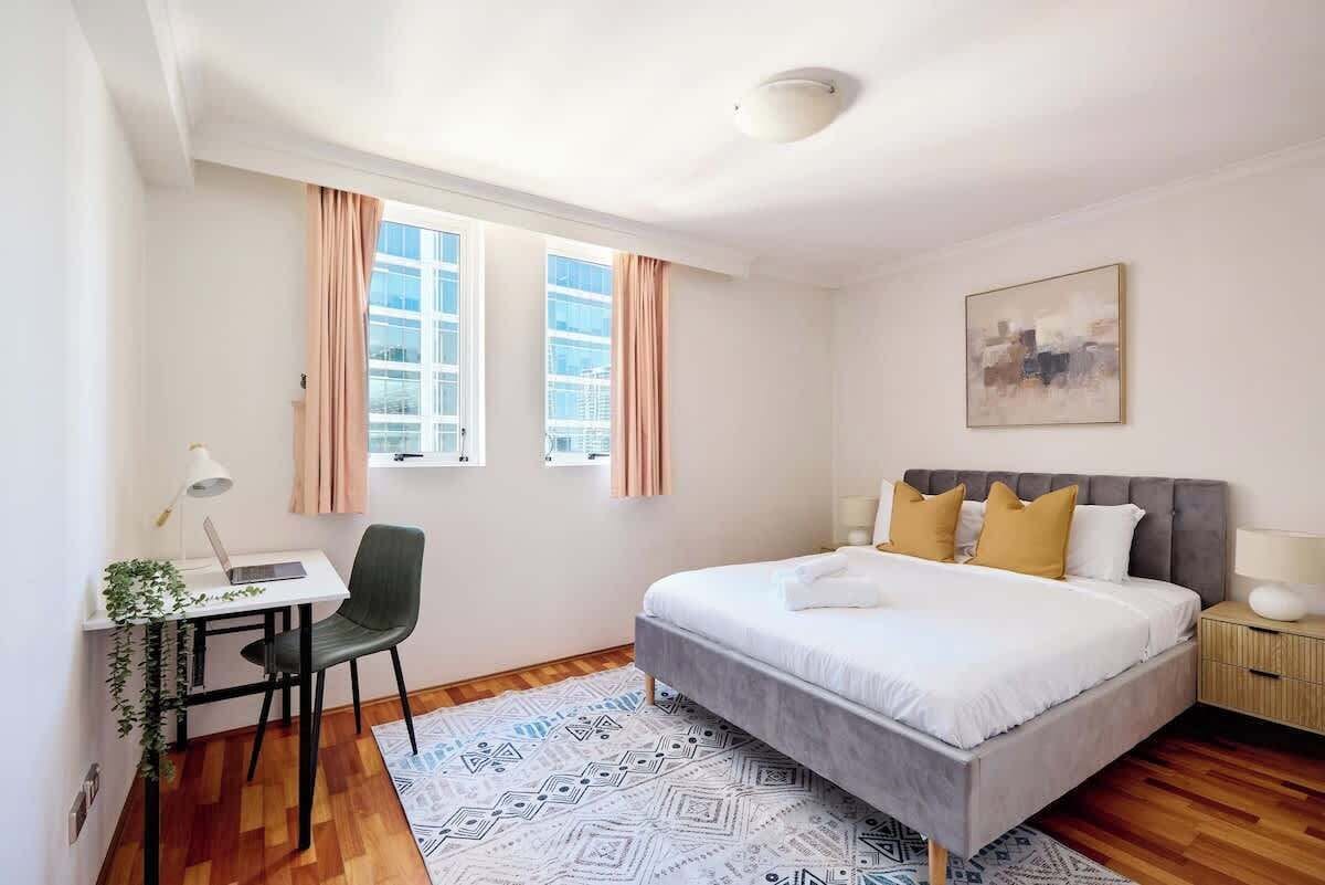 A bedroom with a bed, a desk, a chair, and a window with curtains.