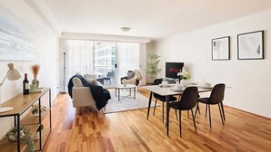Uma sala de estar moderna com área de jantar, um sofá, uma mesa de centro e uma TV fixada na parede.