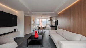 A modern living room with a flat-screen TV, a red sculpture, a white sofa, and a dining area with a view. - lEPl Modern Apt, AC, Nice View, Balcony, Provenza (Medellín)