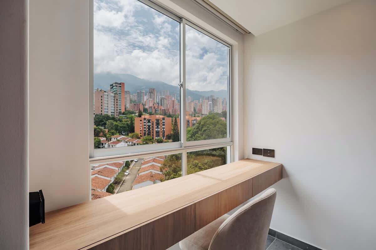 A modern room with a large window, a wooden desk, and a chair.