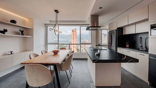 A modern kitchen with a central island, a dining area with chairs, and a view of tall buildings through large windows. - lEPl Modern Apt, AC, Nice View, Balcony, Provenza (Medellín)