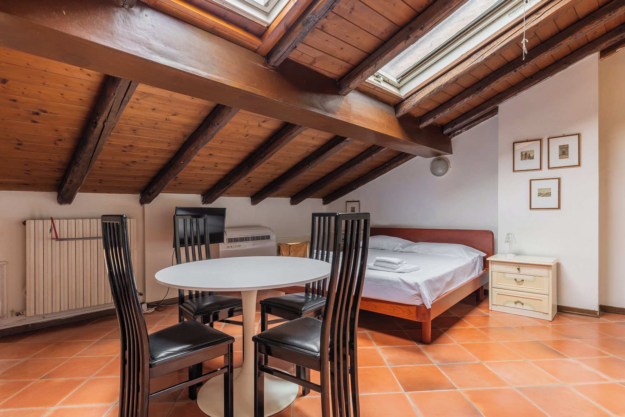 A cozy room with a wooden ceiling, a round table with chairs, a bed, and a small bedside table.