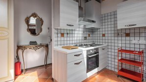 A compact kitchen with a gas stove, oven, and a red metal shelf.