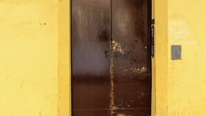 A yellow building with a brown door and a number '23' on the wall.