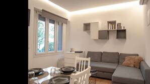 A compact living space with a dining area, a grey sofa, and built-in shelving. - COZY NEW LOFT-CITYLIFE (Milano)