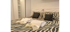Una cama con colcha de estampado de cebra, dos almohadas negras y toallas blancas dobladas con cuidado.