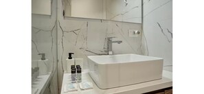 Un baño con lavamanos de mármol blanco, espejo y artículos de aseo.