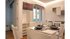 A modern room with a dining table set for two, a white wardrobe, and a sign indicating a Netflix service. - COZY NEW LOFT-CITYLIFE (Milano)