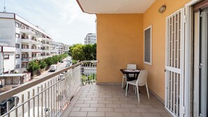 A balcony with a table and chairs, a view of the street, and a building with multiple floors in the background. - Roomy Family Apartment by Wonderful Italy (Bari)