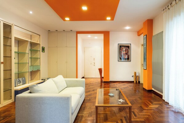 A living room with a sofa, glass coffee table, wooden floor, and a wardrobe with glass doors.