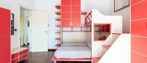 Une petite pièce avec un lit superposé, une armoire rouge et une porte blanche.