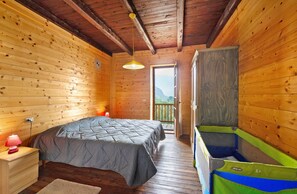 Une chambre à coucher dans une cabane en bois, avec un lit, une table de chevet, une lampe, une fenêtre et une vue sur l’extérieur.