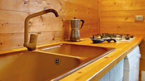 Interior de una cabaña de madera con una cocina que incluye un lavamanos doble, una cafetera y una estufa.