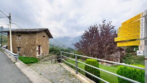 Un edificio de piedra con una escalera que conduce a una carretera, rodeado de vegetación y con una montaña al fondo.