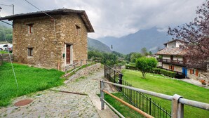 Un edificio de piedra con puerta y ventanas de madera, una escalera de piedra y un área verde con una cerca.
