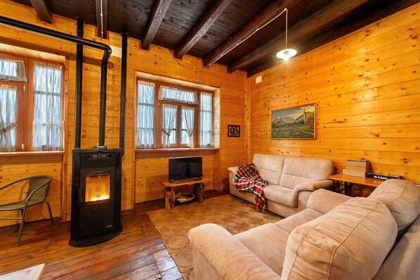 A cozy cabin with a wood-burning stove, a sofa, a television, and a painting on the wall. - La Vieille Ecole Holiday Home – Historic Schoolhouse Retreat in Montjovet (Montjovet)