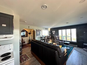 A modern living room with a black leather sofa, a dining area with a table and chairs, and a kitchen with a stove. - Stunning 1BR Bird Island Overlook near Klondike Trail in Elliston (Elliston)