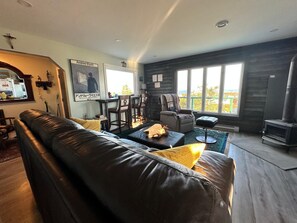 A cozy living room with a leather sofa, a fireplace, and a large window offering a view of the outdoors. - Stunning 1BR Bird Island Overlook near Klondike Trail in Elliston (Elliston)
