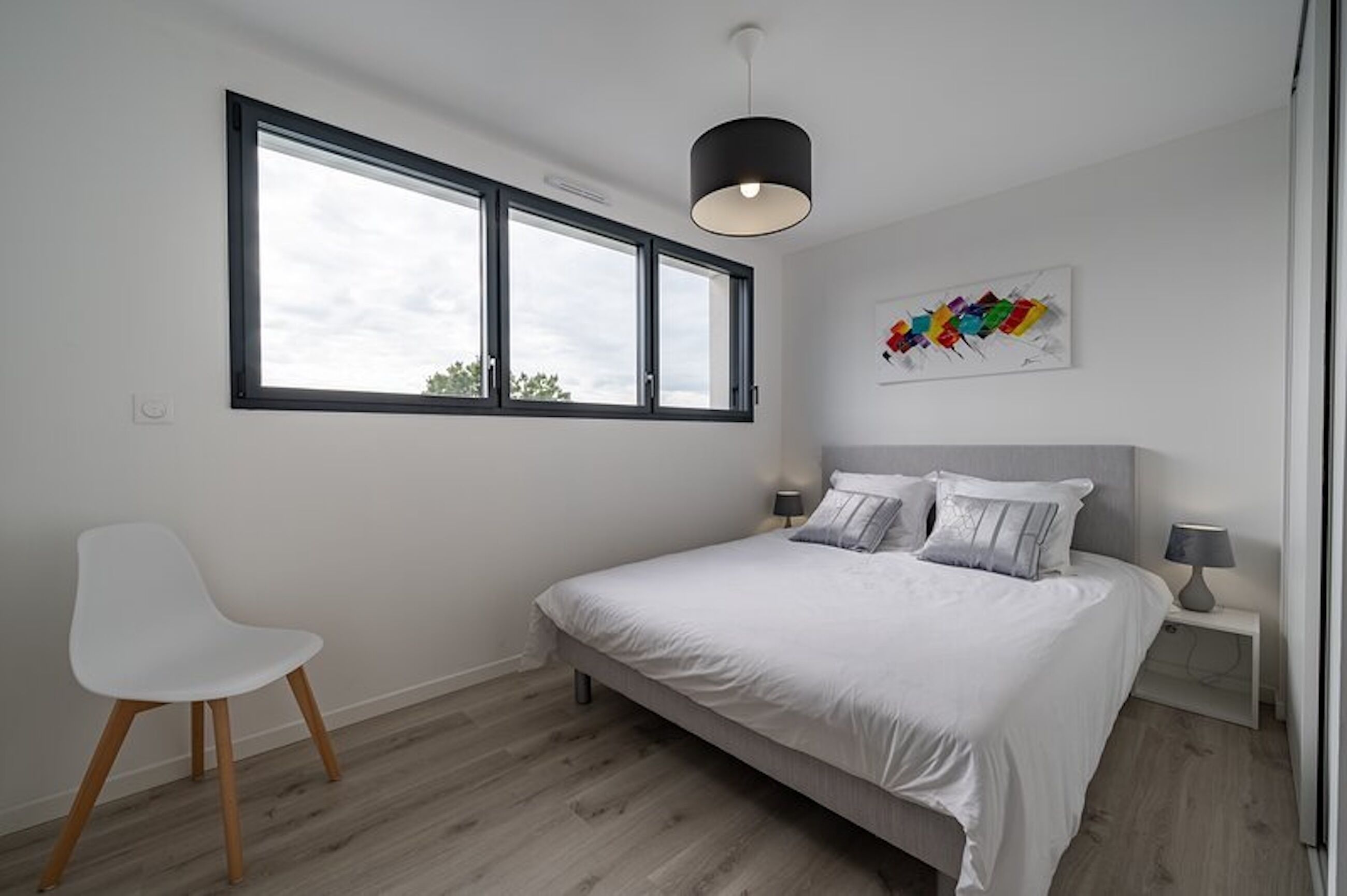 A bedroom with a bed, a chair, a window, and a wall art piece.