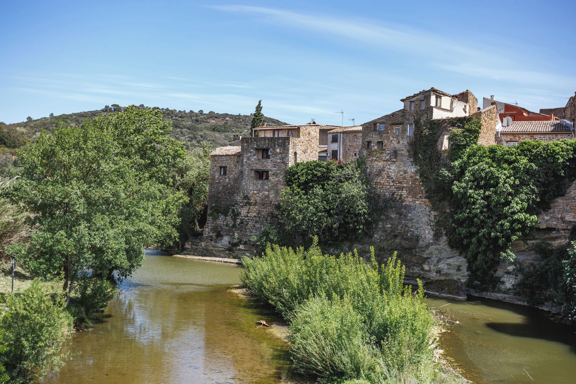 Ein historisches Steinhaus mit einem Fluss davor, umgeben von viel Grün.