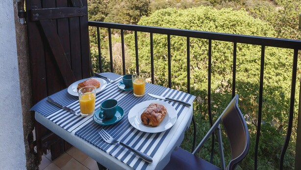 A balcony table with breakfast items and a scenic view. - Cosy Apartment in Ancient Gabian with River and Vineyard Views (Gabian)