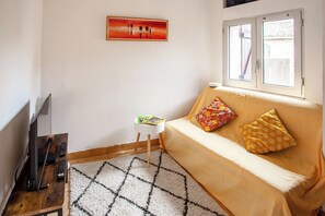 A living room with a sofa, a small table, a TV, and a painting on the wall.