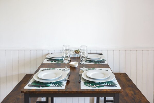 A dining table set with plates, glasses, and cutlery, featuring a tropical leaf pattern on the placemats.