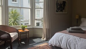 A bedroom with a bed, a chair, a small table with a plant, and a window with curtains. - Peaceful Hastings old town hideaway (Hastings)