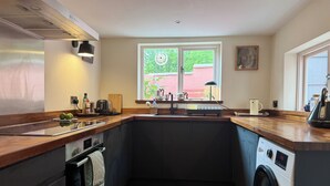 A compact kitchen with a built-in washing machine, a large window with a view, and a wooden countertop. - Peaceful Hastings old town hideaway (Hastings)