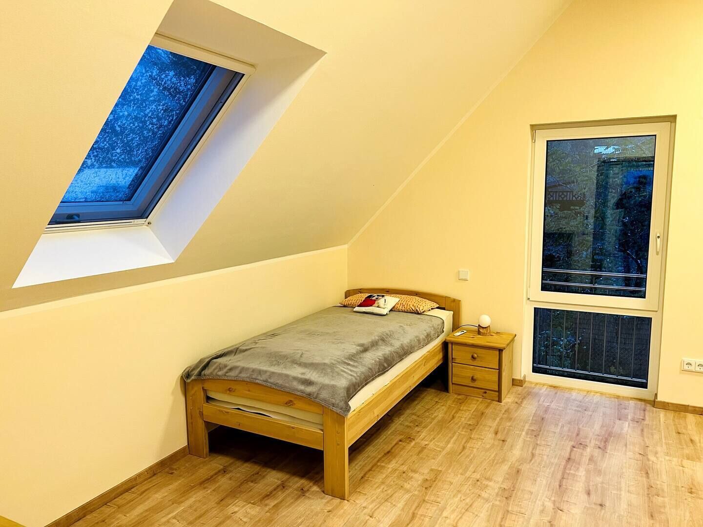 Une chambre avec un plafond en pente, un puits de lumière, un lit, une table de chevet et une fenêtre.